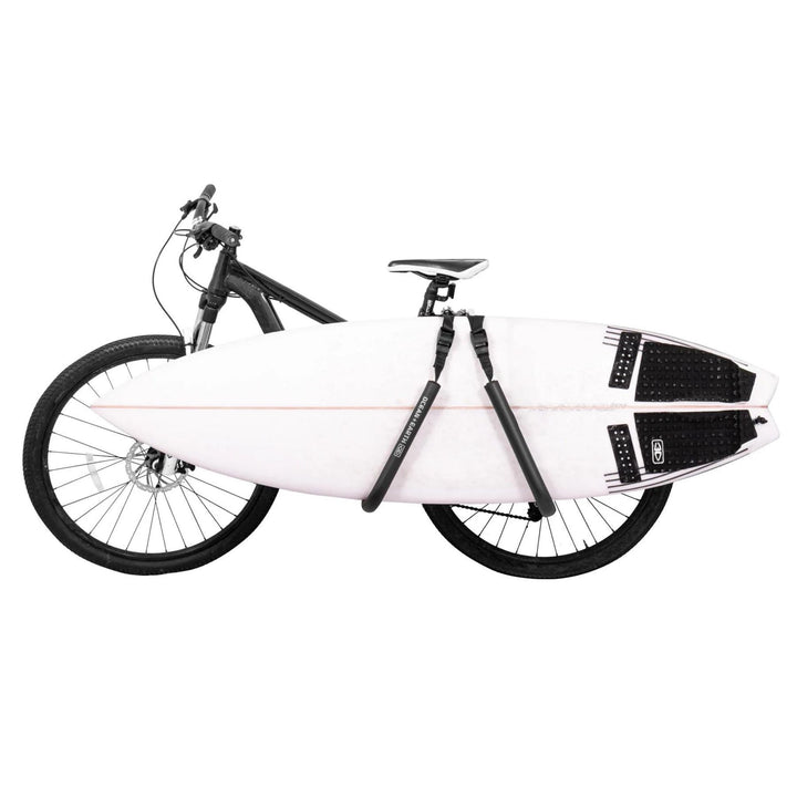 A surfboard rack mounted on a bicycle, with a white surfboard secured in a protective padded case on the back of the bike.